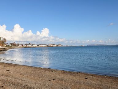 A pebble beach with calm water and a town with buildings in the background at Lluest in Beaumaris