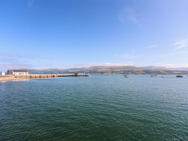 A view of a body of water with a pier and boats with hills in the background at Lluest in Beaumaris