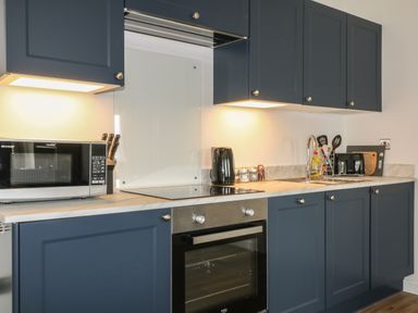 A kitchen with blue cabinets a microwave an oven a kettle a sink and kitchen utensils at Primrose End in Jacobstow