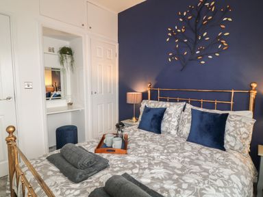 A bedroom with a brass bed frame blue accent wall and a dressing table at Primrose End in Jacobstow