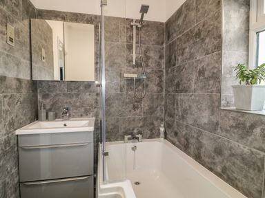 A bathroom with a bathtub shower sink cabinet and a plant on the windowsill at Primrose End in Jacobstow
