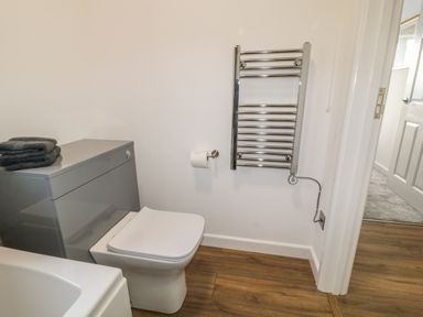 A bathroom with a toilet a towel rack with electric cord folded towels on toilet tank and wooden floor at Primrose End in Jacobstow
