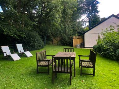 A garden with wooden table and chairs and two white reclining chairs at Primrose End in Jacobstow