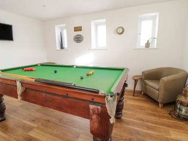A game room with a pool table a wall clock a chair a small table and a mounted television at The Bull Inn in Deiniolen