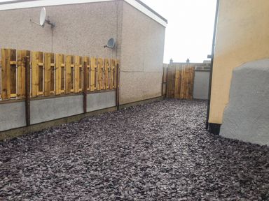 An outdoor area with slate chippings ground covering wooden fences on the side and walls of adjacent buildings at The Bull Inn in Deiniolen