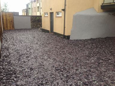 A backyard with purple gravel ground covering next to a yellow building with a door and windows at The Bull Inn in Deiniolen