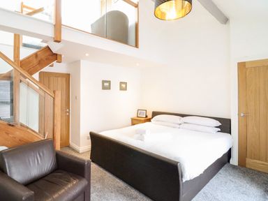 A bedroom with a bed pillows armchair and wooden staircase at The Bull Inn in Deiniolen
