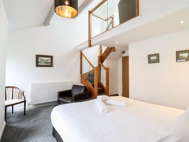 A bedroom with a bed and rolled towels two chairs and a staircase with glass panels at The Bull Inn in Deiniolen