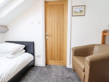 A bedroom with a bed a wooden door and a brown armchair at The Bull Inn in Deiniolen
