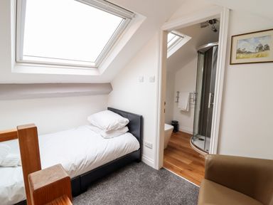 A bedroom with a single bed next to a skylight window and an open door leading to a bathroom with a shower at The Bull Inn in Deiniolen