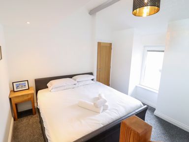 A bedroom with a double bed white bedding and rolled towels on top a bedside table with a picture frame and a window at The Bull Inn in Deiniolen