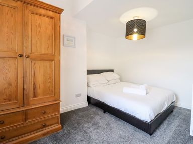 A bedroom with a double bed with white linens and a wooden wardrobe at The Bull Inn in Deiniolen