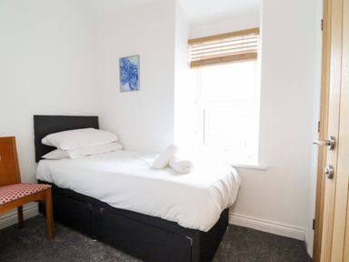 A small bedroom with a single bed a chair a window with blinds and a painting on the wall at The Bull Inn in Deiniolen