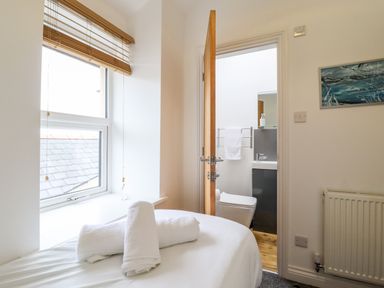 A bedroom with a window and rolled towels on a bed next to a bathroom door at The Bull Inn in Deiniolen