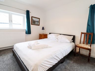 A bedroom with a double bed pillows and folded towels bedside table with lamp wooden chair and window with dark curtains at The Bull Inn in Deiniolen