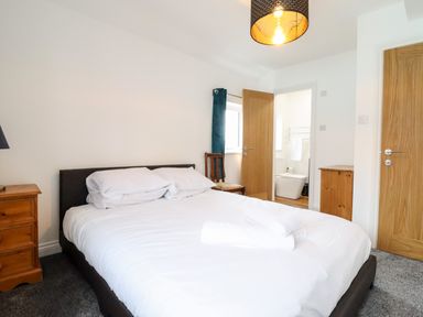 A bedroom with a double bed wooden furniture and an open door leading to a bathroom at The Bull Inn in Deiniolen