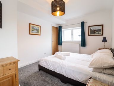A bedroom with a double bed towels on the bed curtains on the window bedside table with lamp and wooden dresser at The Bull Inn in Deiniolen