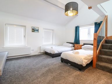 A bedroom with two single beds a wooden nightstand two windows and carpeted stairs at The Bull Inn in Deiniolen