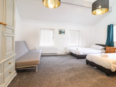 A bedroom with two single beds a gray sofa cabinet and windows at The Bull Inn in Deiniolen