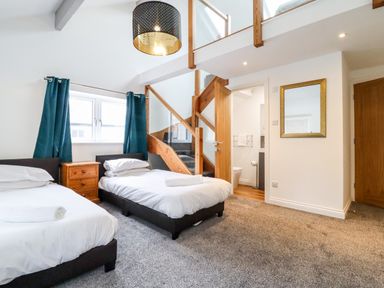 A bedroom with two single beds a wooden nightstand a staircase with wooden railing and a mirror on the wall at The Bull Inn in Deiniolen