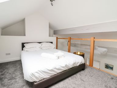 A bedroom with a bed and towels on a gray carpet with a wooden and glass railing at The Bull Inn in Deiniolen