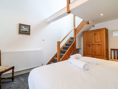 A bedroom with a bed with rolled towels a wooden wardrobe a chair stairs and white walls at The Bull Inn in Deiniolen