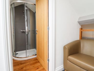 A shower enclosure with glass doors in a small room next to a beige armchair at The Bull Inn in Deiniolen