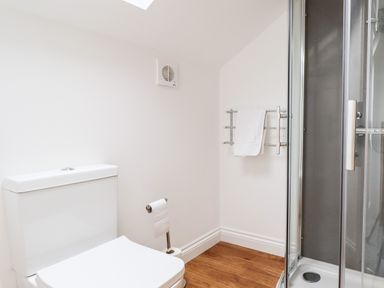 A bathroom with a toilet, a shower with glass doors, a towel rack with a towel, and a wooden floor at The Bull Inn in Deiniolen