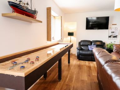 A game room with a shuffleboard table black leather chair brown leather sofa wall mounted TV and model ship on shelf at The Bull Inn in Deiniolen