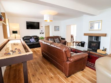 A living room with leather sofas a shuffleboard table a wall mounted television and a fireplace at The Bull Inn in Deiniolen