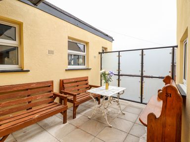 An outdoor patio with wooden benches a white metal table with flowers and yellow walls at The Bull Inn in Deiniolen