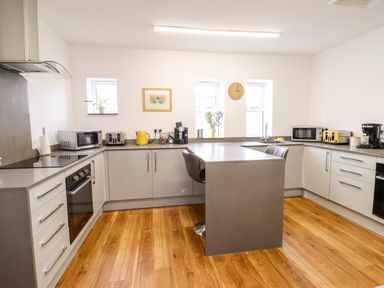 A kitchen with an island and two chairs a microwave a toaster a coffee maker and a clock on the wall at The Bull Inn in Deiniolen