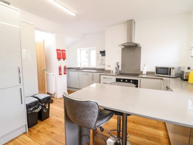 A kitchen with a countertop island and two chairs a stove a microwave and trash bins at The Bull Inn in Deiniolen