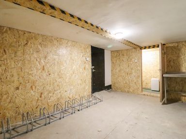 An empty room with plywood walls a metal bike rack a black door and an open wooden door showing a small adjoining room at The Bull Inn in Deiniolen
