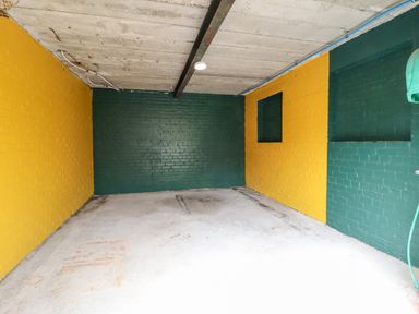 An empty room with yellow and green painted brick walls and a concrete floor at The Bull Inn in Deiniolen