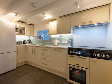 A kitchen with cream cabinets a refrigerator microwave oven and teal tiled backsplash at Rose Cottage in St Ives