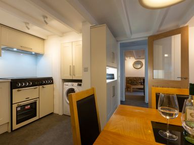 A kitchen with an oven washing machine cabinets and dining table with wine glasses at Rose Cottage in St Ives