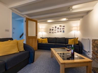 A seating area with two dark sofas with yellow cushions a wooden coffee table with wine glasses and bottle and lamps at Rose Cottage in St Ives