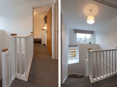 A carpeted stairway and landing with white wooden railings and a window at Rose Cottage in St Ives