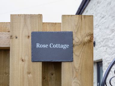 A wooden fence with a dark rectangular sign that reads Rose Cottage at Rose Cottage in St Ives