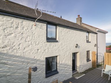 Exterior view of a stone house with black framed windows and a small fenced patio area at Rose Cottage in St Ives