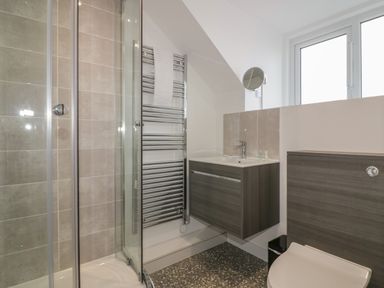 A bathroom with a glass shower enclosure a wall-mounted sink unit a heated towel rail and a toilet at Rose Cottage in St Ives