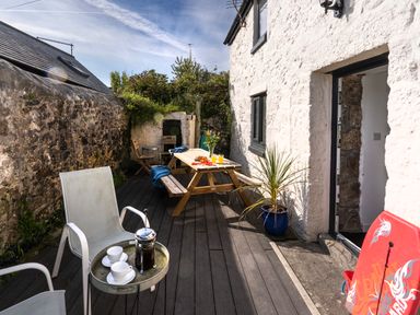 A patio with chairs table and cups near a white stone wall at Rose Cottage in St Ives