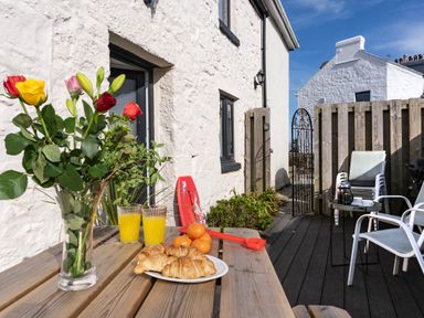An outdoor patio with a wooden picnic table holding flowers croissants orange juice and mandarins at Rose Cottage in St Ives
