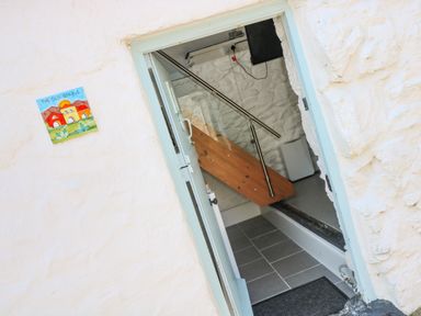 An entryway with a door open showing a stairway with metal handrails inside a white stone building at The Old Stable in Porthallow