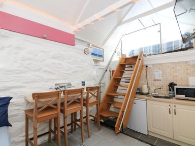 A kitchen area with wooden stools and a small staircase leading to a loft bed at The Old Stable in Porthallow