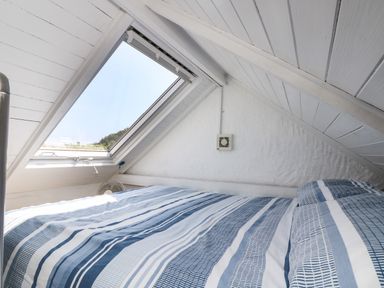 A bedroom with a slanted ceiling skylight window and a bed with striped bedding at The Old Stable in Porthallow