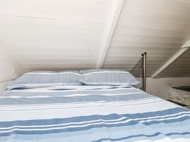 A bed with blue and white striped bedding under a white slanted ceiling at The Old Stable in Porthallow