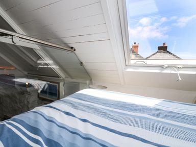 A bedroom with a striped blue and white bedspread under a skylight window at The Old Stable in Porthallow