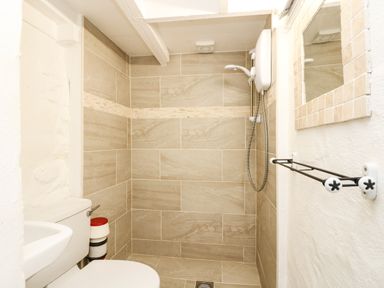 A bathroom with a toilet sink tiled shower and a towel rack at The Old Stable in Porthallow